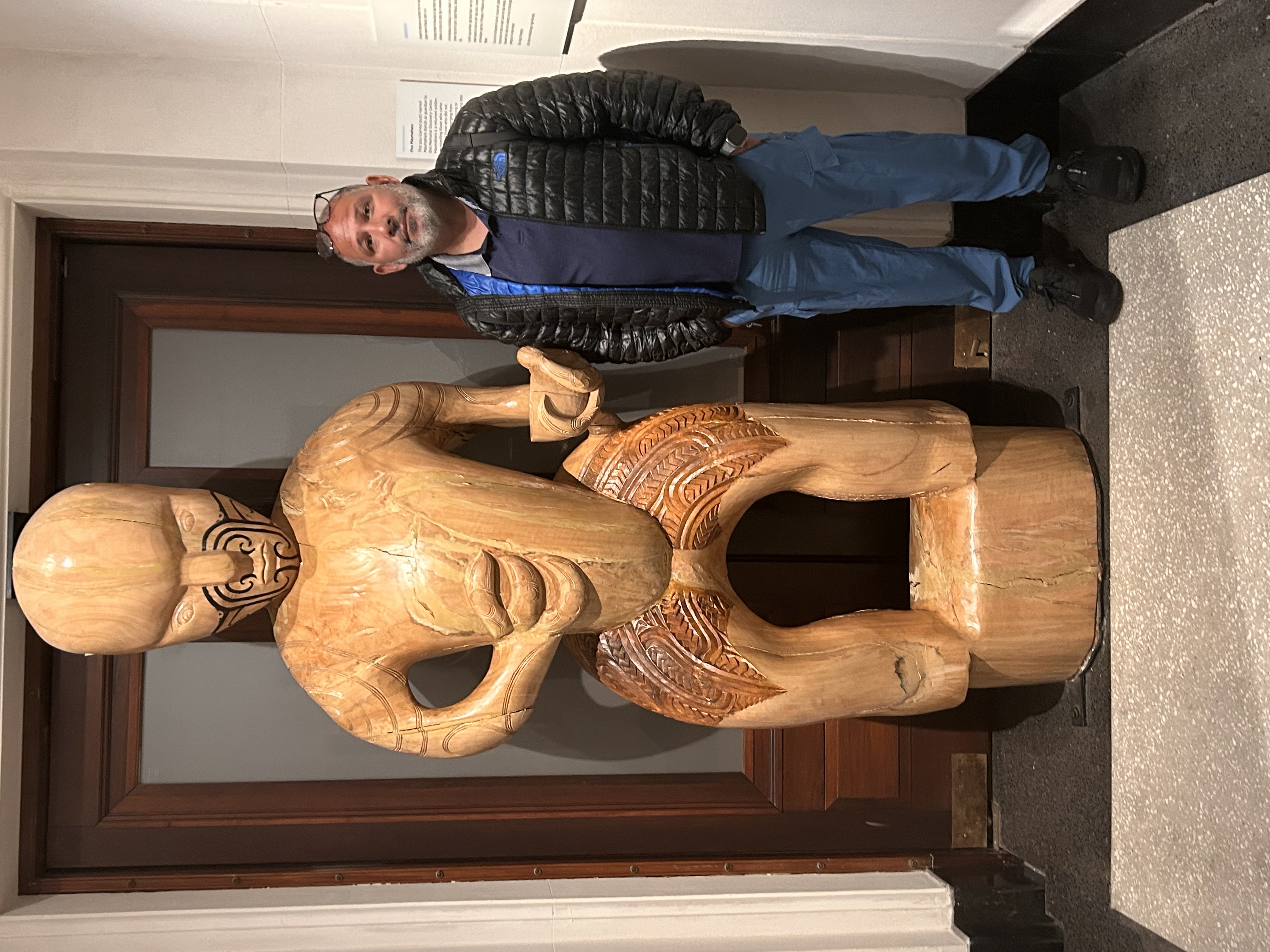 Hiram standing beside a large Māori carved figure inside Auckland Museum